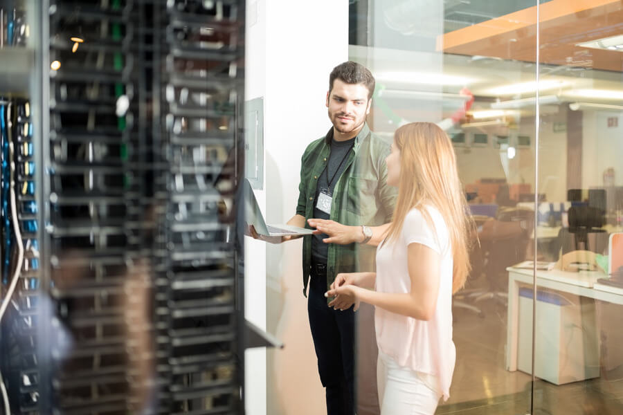 Two people standing inside a server room, talking to each other.